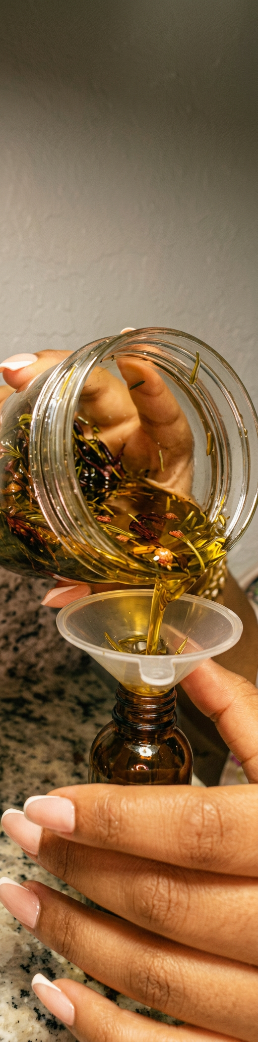 Pouring herb-infused hair oil through a funnel into an amber bottle